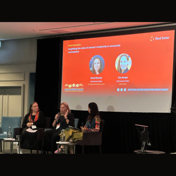 Woman speaking on a panel at a Third Sector conference, with a presentation slide behind the panellists titled "Amplifying the value of women's leadership in community and business.